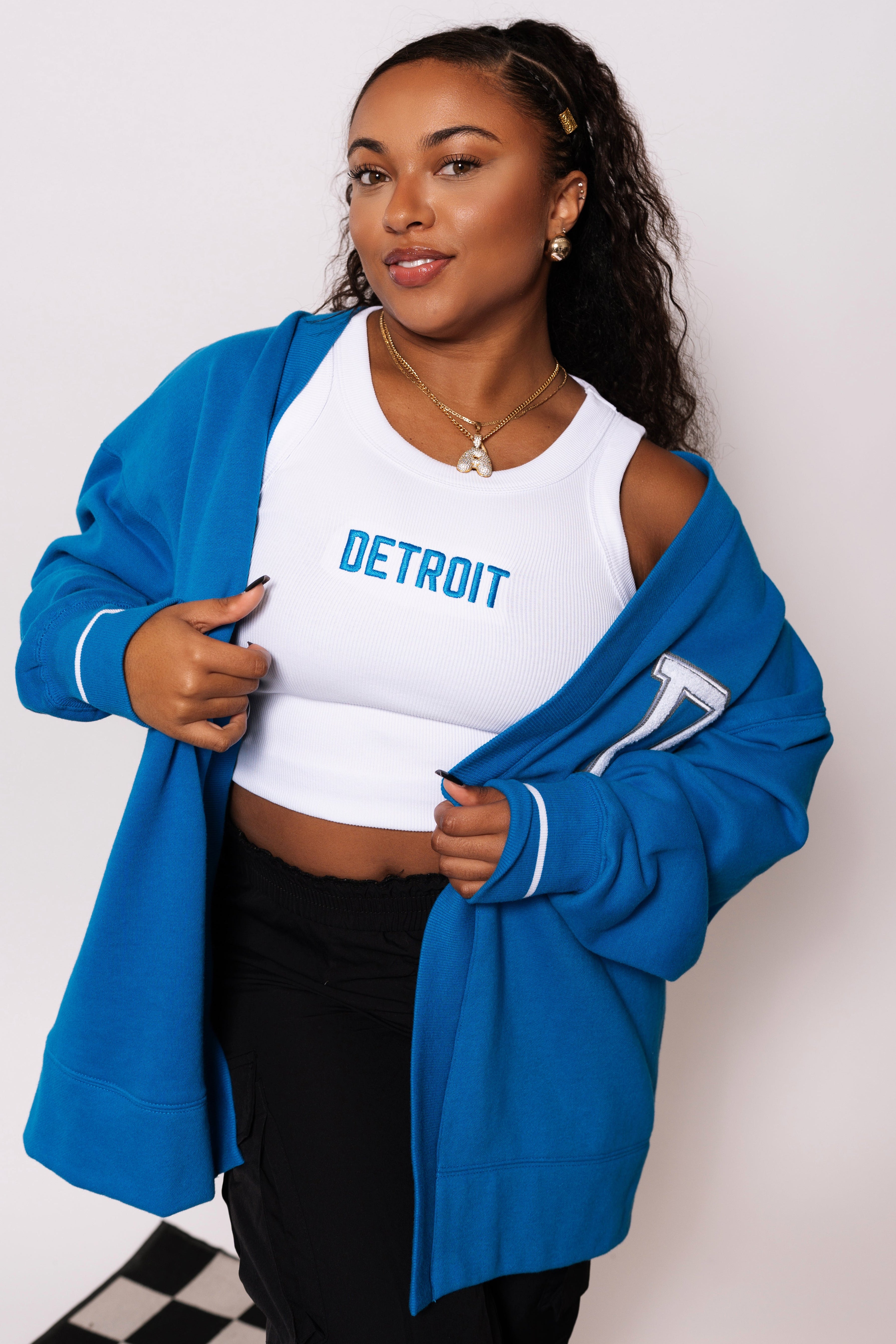Woman wearing a blue cardigan over a white crop top with 'Detroit' text on a plain background