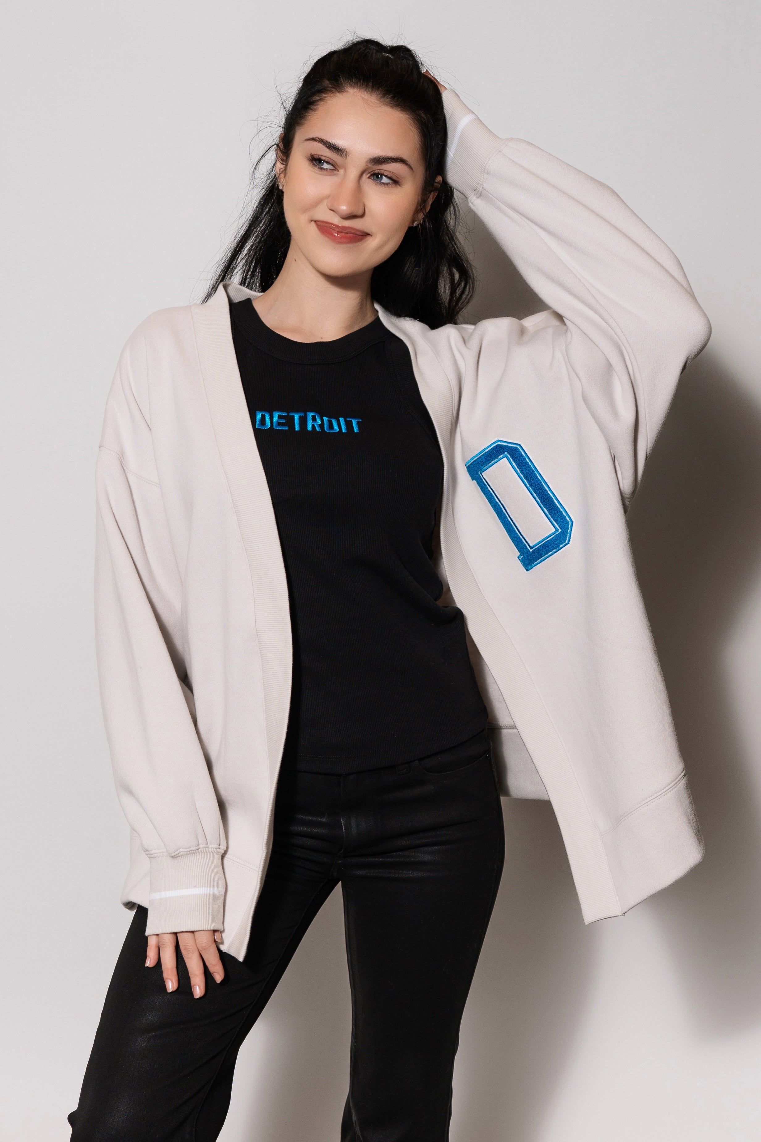 Person wearing a black t-shirt with blue text, black pants, and a light-colored jacket with a blue logo on a checkered floor.