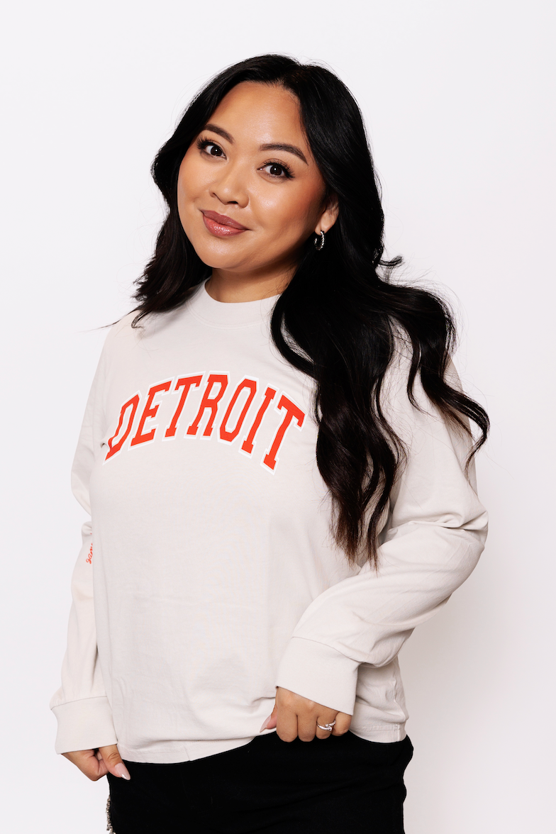 Person wearing a white sweatshirt with 'Detroit' printed in red on a plain background